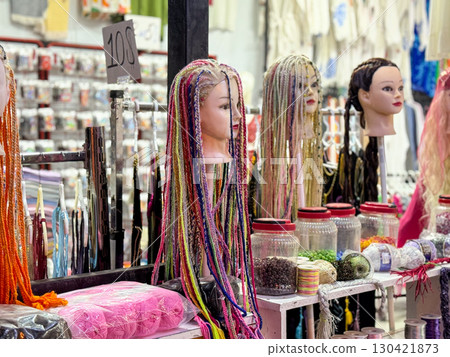 Row of mannequin heads with braided hair in colorful yarn on a market stand. Fashion, hairstyle and consumer culture expressed through creativity, retail and artistic identity. 130421873