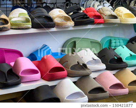 Shelves of colorful plastic sandals and slippers arranged in rows in a store. Fashion, consumer economy and summer leisure expressed through footwear, retail and everyday lifestyle. Shelves of colorful plastic sandals and slippers arranged in rows in a store. Fashion, consumer economy and summer leisure expressed through footwear, retail and everyday lifestyle. 130421877