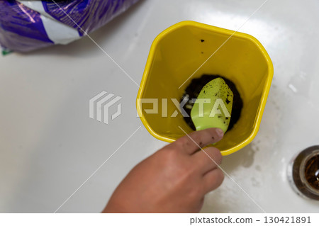 Yellow floral plastic flower pot being filled with soil using small trowel Yellow floral plastic flower pot being filled with soil using small trowel 130421891
