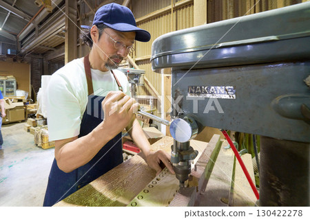 Woodworker drilling holes in wood with a drill press 130422278