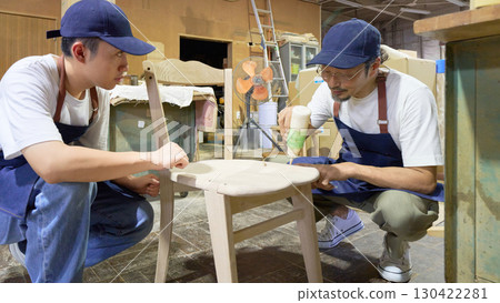 Teamwork between a craftsman and apprentice finishing a chair in a woodworking shop 130422281