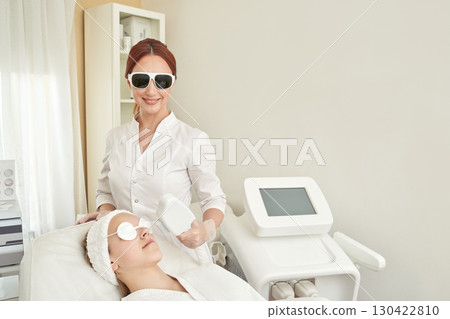 Caucasian female spa professional performing facial laser treatment on young Caucasian female spa professional performing facial laser treatment on young 130422810