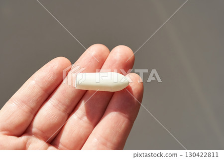 Hand holding white medical suppository for relief and treatment on neutral Hand holding white medical suppository for relief and treatment on neutral 130422811