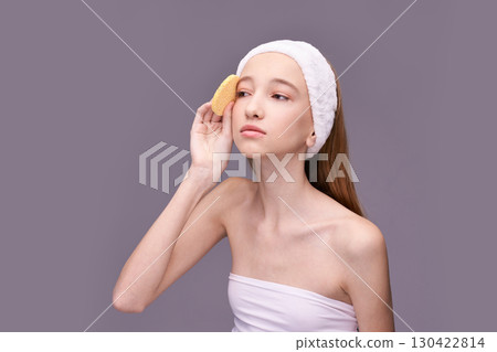 Young caucasian female teen with headband using skincare sponge against purple 130422814