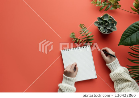 Aerial view of woman s hands in white sweater taking notes in spiral notebook on orange background 130422860