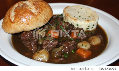 A white plate of beef bourguignon with tender beef cubes, carrots, and pearl onions in a rich wine sauce, served with a crusty roll and garlic bread 130423095