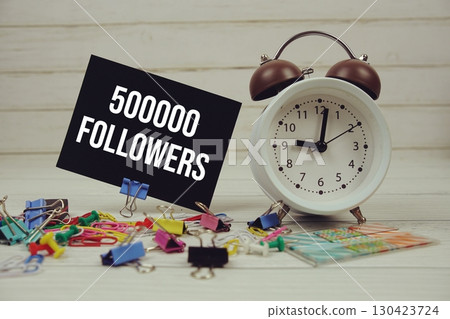 500000 Followers text on paper card with alarm clock and stationary on wooden background 130423724