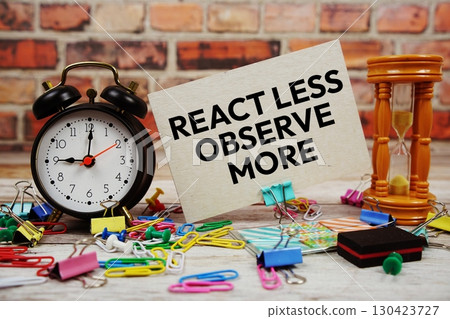 React Less Observe More text on paper card with alarm clock and stationary on wooden background 130423727