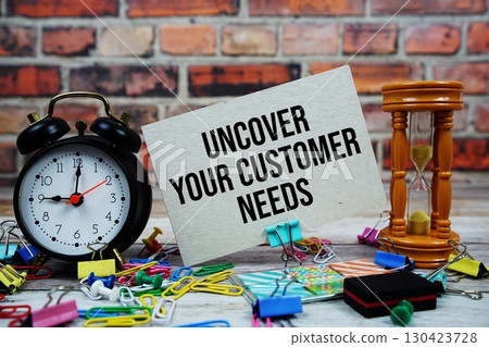 Uncover Your Customer Needs text on paper card with alarm clock and stationary on wooden background 130423728