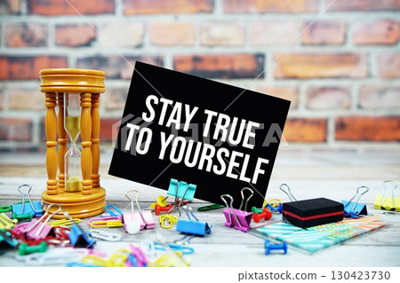 Stay True To Yourself text on paper card with hourglass and stationary on wooden background 130423730