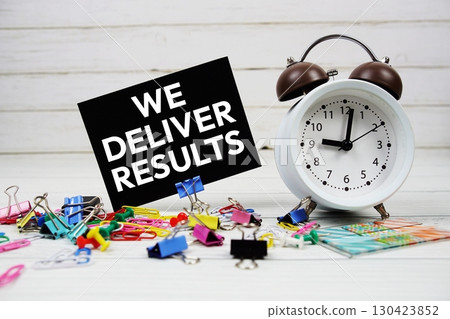 We Deliver Results text on paper card with alarm clock and stationary on wooden background We Deliver Results text on paper card with alarm clock and stationary on wooden background 130423852