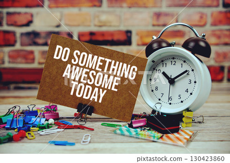 Do Something Awesome Today text on paper card with alarm clock and stationary on wooden background Do Something Awesome Today text on paper card with alarm clock and stationary on wooden background 130423860