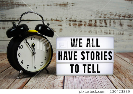 We all have stories to tell text on light box with alarm clock on wooden background 130423889