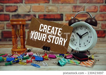 Create Your Story text on paper card with alarm clock and stationary on wooden background 130423897