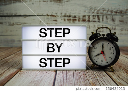 Step by Step text on light box with alarm clock on wooden background 130424013