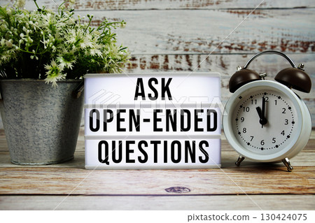 Ask Open-Ended Questions text on light box with alarm clock on wooden background 130424075