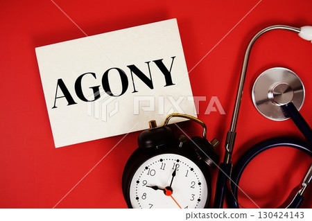 Agony text written on paper card with stethoscope and alarm clock on red background 130424143