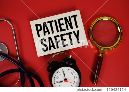 Patient Safety text written on paper card with stethoscope, alarm clock and magnifying glass red background 130424154