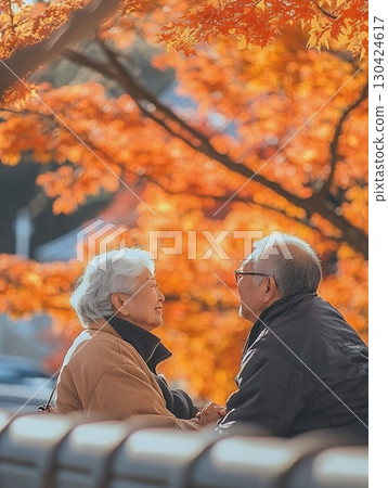 An elderly couple enjoys a peaceful moment in a park, surrounded by vibrant autumn leaves and a warm atmosphere 130424617