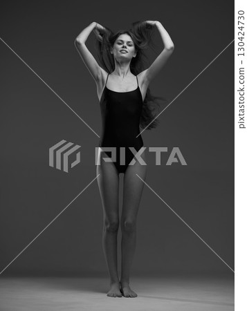 Black and white portrait of a slim woman in a black swimsuit with long hair and confident expression. 130424730
