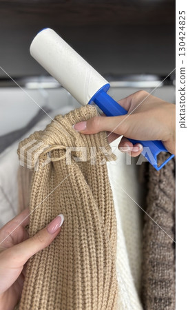 Woman using lint roller to clean lint laden clothes in closet, removing dust and debris from fabric. Wardrobe organization, clothing care, fashion and hygiene concept. Womens clothing maintenance Woman using lint roller to clean lint laden clothes in closet, removing dust and debris from fabric. Wardrobe organization, clothing care, fashion and hygiene concept. Womens clothing maintenance 130424825