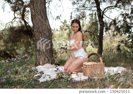 Picnic Flowers Woman: Woman kneels, holding daisies in sunny woods, enjoying a peaceful daytime picnic. Picnic Flowers Woman: Woman kneels, holding daisies in sunny woods, enjoying a peaceful daytime picnic. 130425011