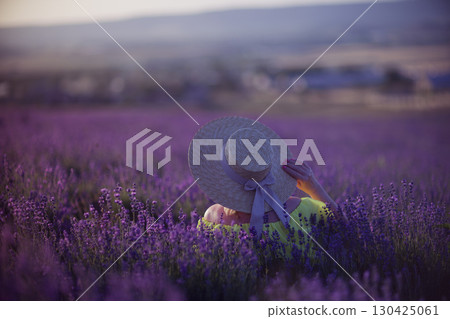 Lavender Woman Hat: Back view in field at sunset, holding flowers, serene moment. 130425061