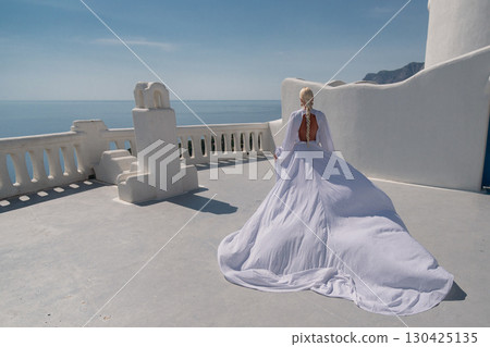 Santorini Gown Balcony: Woman in white dress poses on sunny terrace overlooking Aegean Sea. 130425135