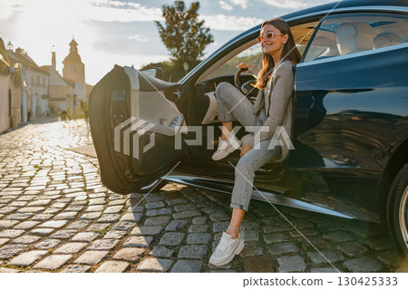 A Stylish Woman Taking a Moment to Relax by a Luxury Car under the Beautiful Sunset Glow A Stylish Woman Taking a Moment to Relax by a Luxury Car under the Beautiful Sunset Glow 130425333