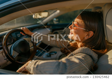 A Young Woman Happily Enjoying a Drive in a Luxurious and Stylish Car Beneath a Golden Sunset A Young Woman Happily Enjoying a Drive in a Luxurious and Stylish Car Beneath a Golden Sunset 130425462