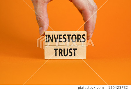 Investors trust symbol. Concept words Investors trust on wooden blocks on a beautiful orange table orange background. Businessman hand. Business invest and investors trust concept, copy space. 130425782