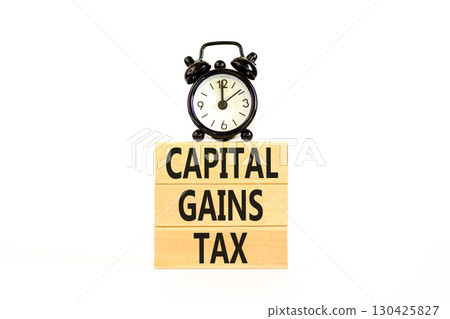 Capital gains tax symbol. Concept words Capital gains tax on beautiful wooden block. Black alarm clock. Beautiful white background. Business and capital gains tax concept. Copy space. 130425827