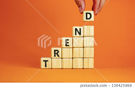 Trend and trending symbol. Concept word Trend on beautiful wooden blocks. Beautiful orange table orange background. Businessman hand. Business lifestyle trend and trending concept. Copy space. 130425868