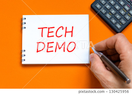 Tech demo symbol. Concept word Tech demo on beautiful white note. Businessman's hand. Black calculator. Beautiful orange paper background. Business tech demo concept. Copy space. 130425956
