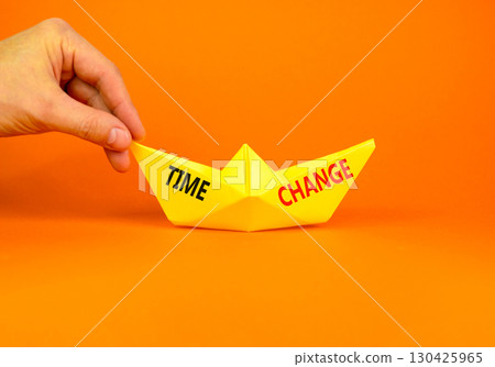 Time change symbol. Concept word Time change on beautiful yellow paper boat. Businessman's hand. Beautiful orange paper background. Business time change concept. Copy space. Time change symbol. Concept word Time change on beautiful yellow paper boat. Businessman's hand. Beautiful orange paper background. Business time change concept. Copy space. 130425965