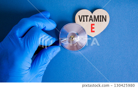 Vitamin E tocopherols symbol. Concept words Vitamin E on beautiful wooden heart. Doctor's hand in blue medical glove. Beautiful blue background. Medical healthy lifestyle Vitamin E tocopherols concept 130425980