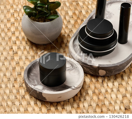 Black metal cosmetic jars and tubes on a decorative tray. Minimalism, skin care, stylish beauty background for brand presentation. Black metal cosmetic jars and tubes on a decorative tray. Minimalism, skin care, stylish beauty background for brand presentation. 130426218