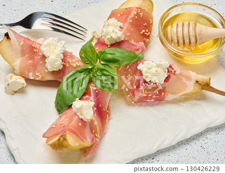 Pear slice wrapped in prosciutto with cheese and sesame seeds on a white board 130426229