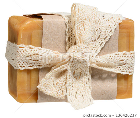 A piece of natural brown soap wrapped in craft paper and tied with a light knitted ribbon tied in a bow. 130426237