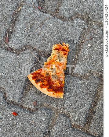 A slice of pizza lying on the pavement outdoors. Street food, waste, and casual moment in everyday urban life. A slice of pizza lying on the pavement outdoors. Street food, waste, and casual moment in everyday urban life. 130426424