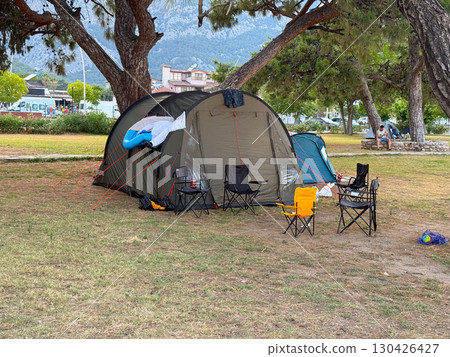 A large camping tent with chairs under pine trees. Outdoor leisure, travel, and family holiday in a mountain camping site. 130426427