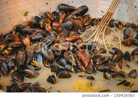 Fresh mussels simmering in aromatic broth inside large pan at street seafood stand. Concept of mussels, seafood flavor, city street cuisine Fresh mussels simmering in aromatic broth inside large pan at street seafood stand. Concept of mussels, seafood flavor, city street cuisine 130426563