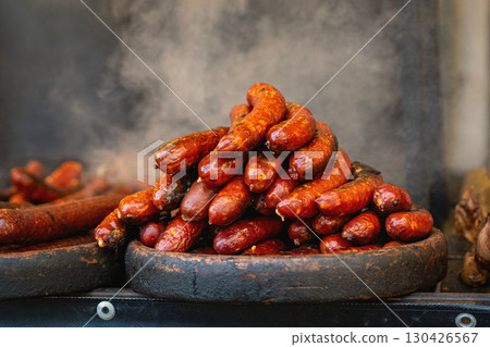 Pile of hot grilled sausages steaming on rustic wooden tray at street food festival. Concept of grilled sausages, local flavor, food abundance Pile of hot grilled sausages steaming on rustic wooden tray at street food festival. Concept of grilled sausages, local flavor, food abundance 130426567