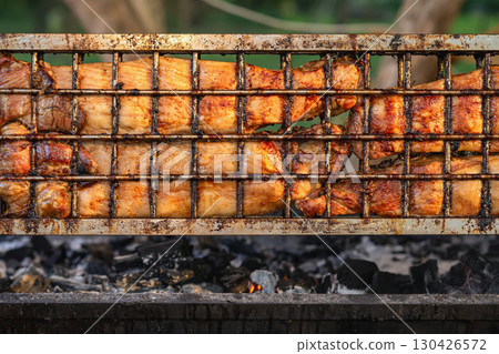Juicy grilled meat sizzling on rotating hot barbecue grill with visible char marks and golden crust. Concept of grilled meat, outdoor barbecue, summer feast Juicy grilled meat sizzling on rotating hot barbecue grill with visible char marks and golden crust. Concept of grilled meat, outdoor barbecue, summer feast 130426572