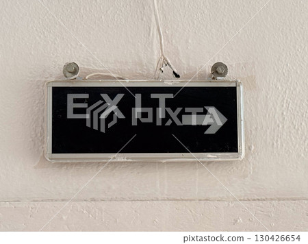 Exit sign with white letters and arrow on black background fixed to wall. Navigation, safety and communication represented through signage, typography and building orientation. Exit sign with white letters and arrow on black background fixed to wall. Navigation, safety and communication represented through signage, typography and building orientation. 130426654