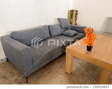 Gray sofa with cushions beside a wooden table holding orange plant. Interior, comfort and lifestyle represented through furniture, decoration and domestic arrangement. Gray sofa with cushions beside a wooden table holding orange plant. Interior, comfort and lifestyle represented through furniture, decoration and domestic arrangement. 130426667