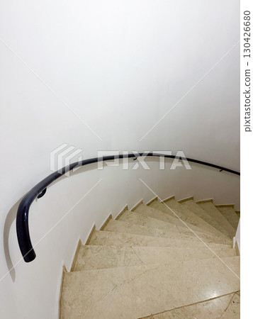 Curved staircase with marble steps and black handrail inside a building. Architecture, movement and function represented through design, geometry and circulation space. Curved staircase with marble steps and black handrail inside a building. Architecture, movement and function represented through design, geometry and circulation space. 130426680