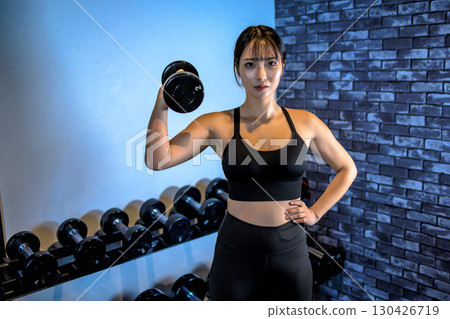 一位女士單手舉起啞鈴。一位酷炫的女士正在健身房鍛鍊。上半身。肌肉訓練女孩。 一位女士單手舉起啞鈴。一位酷炫的女士正在健身房鍛鍊。上半身。肌肉訓練女孩。 130426719