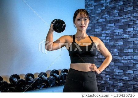 一位女士單手舉起啞鈴。一位酷炫的女士正在健身房鍛鍊。上半身。肌肉訓練女孩。 一位女士單手舉起啞鈴。一位酷炫的女士正在健身房鍛鍊。上半身。肌肉訓練女孩。 130426720