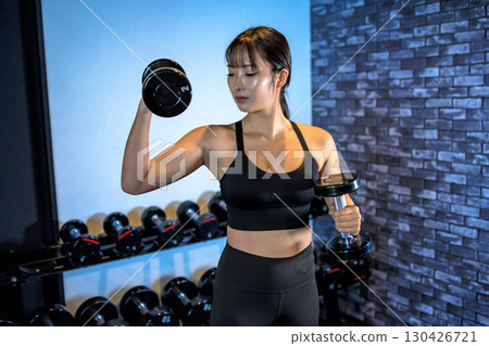 一位女士單手舉起啞鈴。一位酷炫的女士正在健身房鍛鍊。上半身。肌肉訓練女孩。 130426721